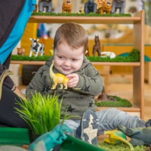 A young boy learning at nursery by playing with toy dinosaurs