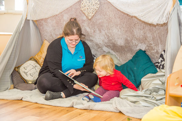 A Child reading a book with a nursery nurse on world book day