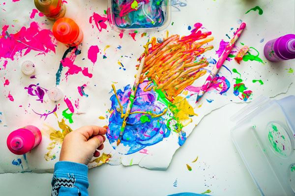 A young child using colourful paints to make finger paintings as part of sensory development.
