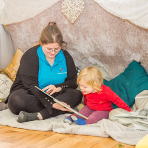 An nursery apprentice reading to a child at Playtime Shepperton